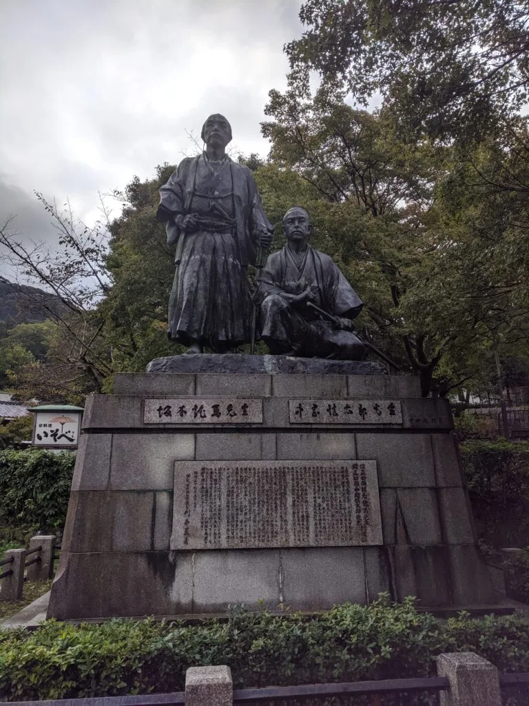 A bronze statue of two historical figures in traditional Japanese attire, displayed at a park in Kyoto.