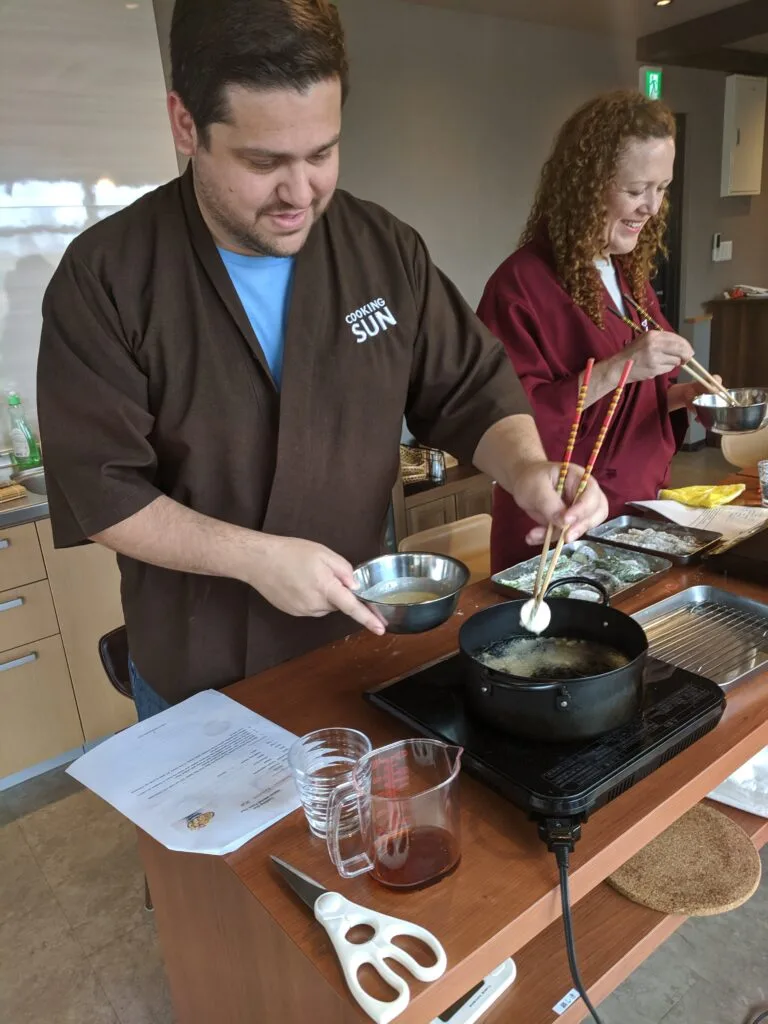 Spencer participating in a cooking class, frying food while wearing a traditional cooking kimono.