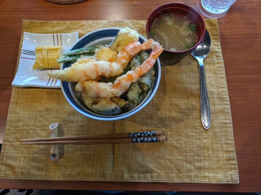 A bowl of tempura with shrimp, vegetables, and miso soup, served with tamagoyaki.
