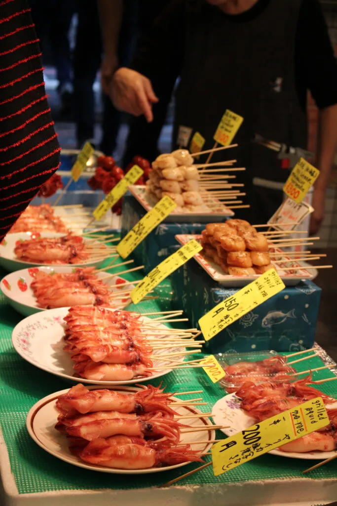 A market display of skewered grilled squid and other food items with price tags.