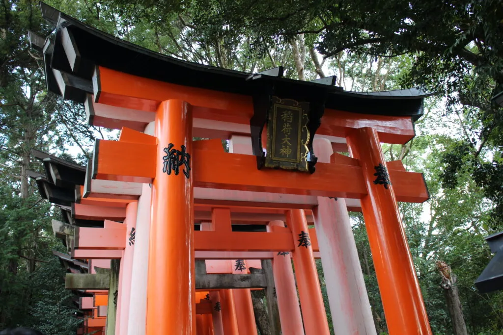 A close-up of the red torii gates at Fushimi Inari Taisha, with a plaque above the entrance.
