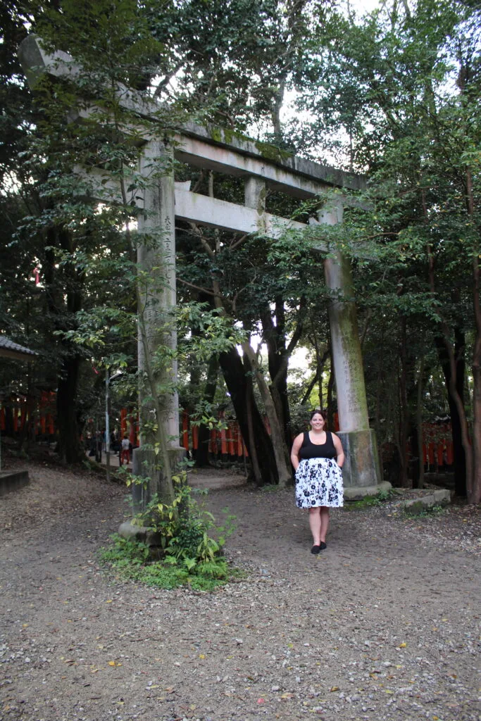 Me, standing beneath a stone torii gate at Fushimi Inari Taisha, surrounded by greenery.