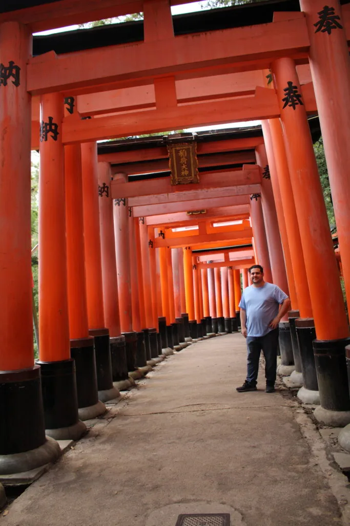 Spencer standing beneath the iconic red torii gates at Fushimi Inari Taisha, framed by rows of gates.