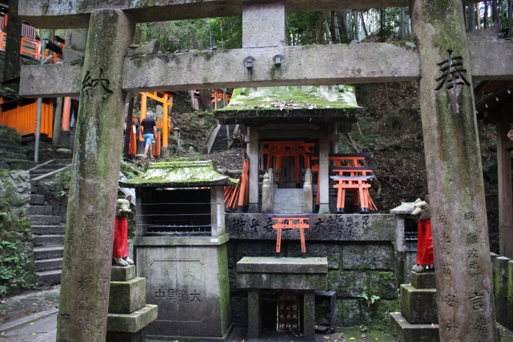 A stone torii gate and small shrine with fox statues at Fushimi Inari Shrine, nestled among the steps and torii gates.