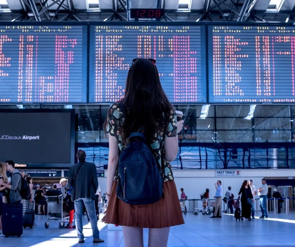 How to Get Through the Airport Quickly: Fly at odd times. Woman standing in front of departure time sign.