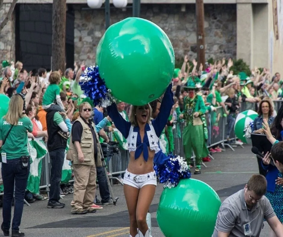 A parade participant in Hot Springs, Arkansas, cheering with a large green beach ball, surrounded by a crowd of people dressed in green.
