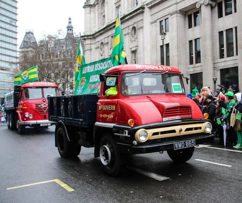 Two vintage trucks decorated with flags in a St. Patrick's Day parade in London.