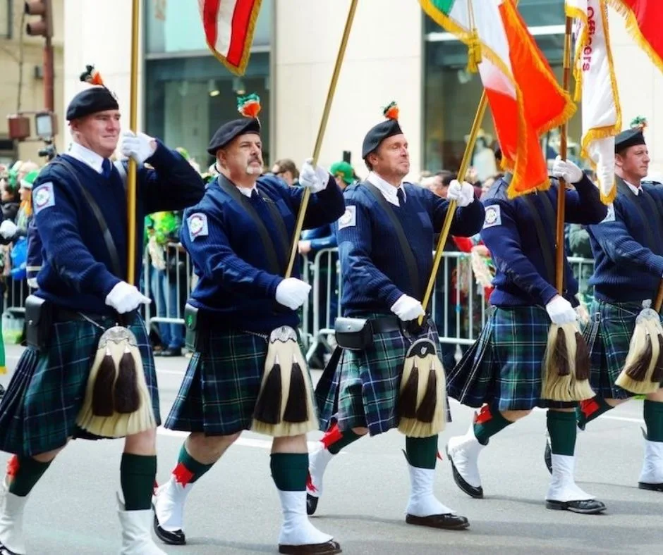 A group of men in kilts marching in a St. Patrick's Day parade, carrying flags in New York City.