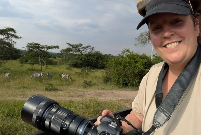 Pamela on safari in the Masai Mara with her camera, zebras grazing behind her